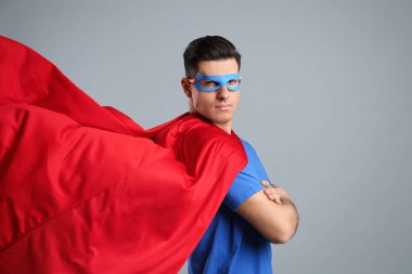 Gri arka planda süper kahraman pelerini ve maskesi giyen adam.