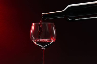 Kırmızı şarap şişeden bardağa koyu arkaplan üzerine dökülüyor, metin için boşluk