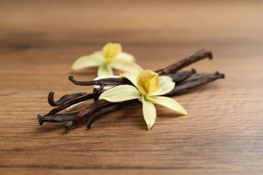 Aromatik vanilya çubukları ve çiçekler ahşap masada, yakın plan.