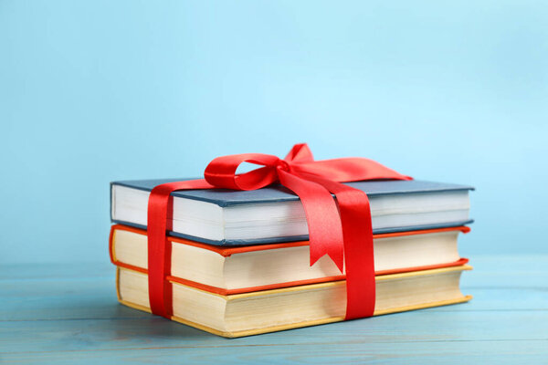 Different books tied with red ribbon on light blue wooden table