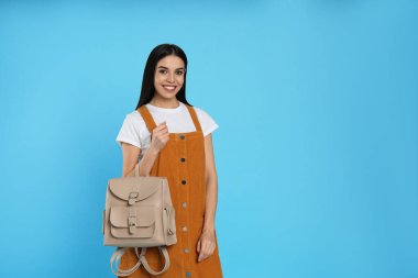 Açık mavi arka planda şık sırt çantalı genç bir kadın. Metin için boşluk