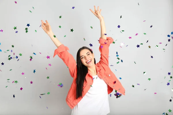 Happy woman and falling confetti on light grey background