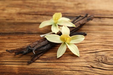 Aromatik vanilya çubukları ve çiçekler ahşap masada, yakın plan.