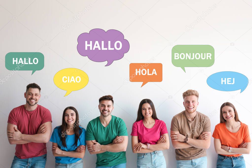 Happy people posing near light wall and illustration of speech bubbles with word Hello written in different languages