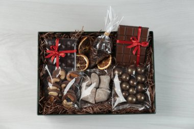 Çikolatalı hediye kutusu ve beyaz ahşap masada tatlılar, üst manzara.