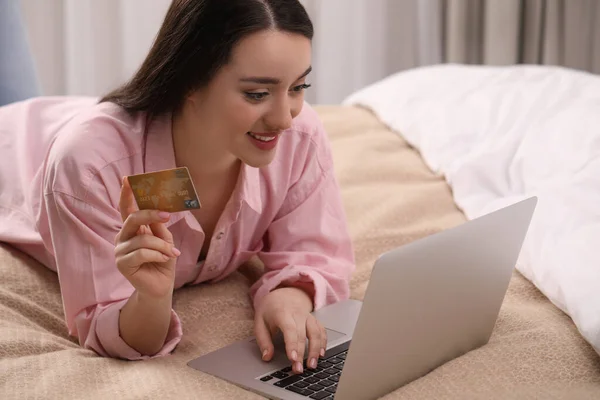 Woman with credit card using laptop for online shopping in bedroom