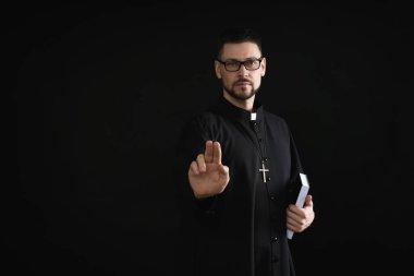 İncil 'i olan bir rahip karanlık arka planda kutsal bir jest yapıyor.