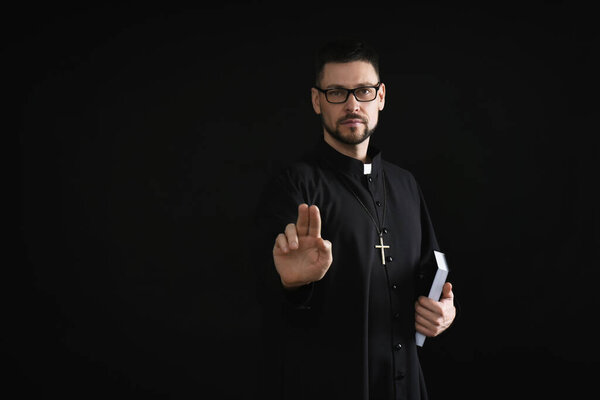 Священник с Библией делает благословенный жест на темном фоне, пространство для текста