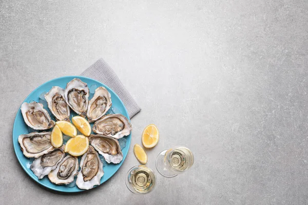 Fresh oysters with lemon and glasses of champagne on grey table, flat lay. Space for text