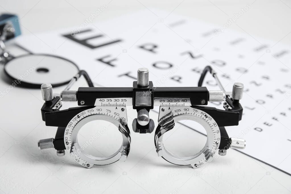 Trial frame, head mirror and eye chart test on white table. Ophthalmologist equipment