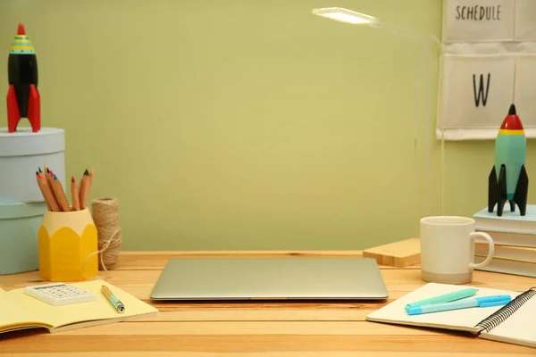 明るい緑の壁の近くの木製の机の上にラップトップと文房具とスタイリッシュな職場 インテリアデザイン — ストック写真