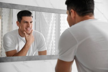 Yakışıklı adam banyoda aynanın yanında tıraş olduktan sonra pürüzsüz yüzüne dokunuyor.