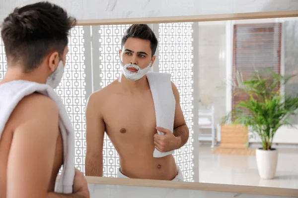 一个英俊的年轻人 浴室里镜子旁边有刮胡子的泡沫 文字的空间 — 图库照片