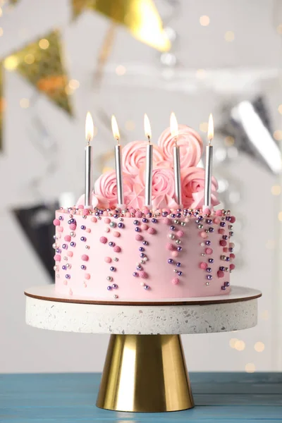 Beautifully decorated birthday cake on turquoise wooden table against blurred festive lights