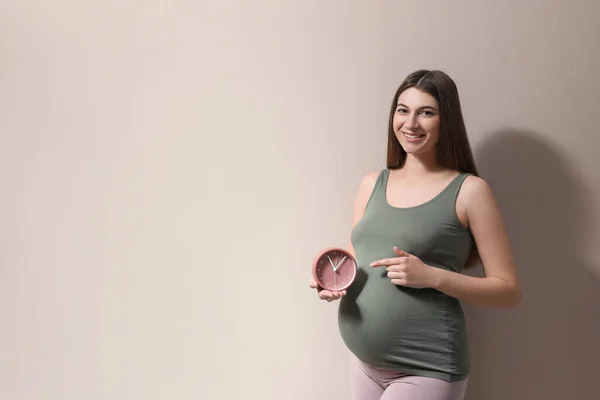 Jovem Grávida Apontando Para Relógio Perto Sua Barriga Fundo Bege — Fotografia de Stock