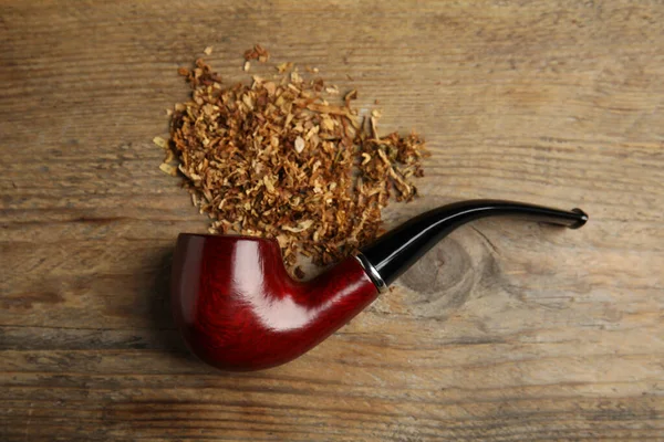 Classic smoking pipe with tobacco on wooden table, flat lay