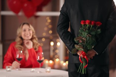 Sevgililer Günü yemeğinde restoranda sevgilisine gül saklayan bir adam.