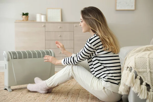 家で電気ヒーターの近くの床に座っている若い女性 — ストック写真