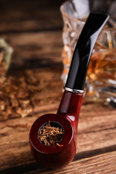 Smoking pipe with tobacco on wooden table