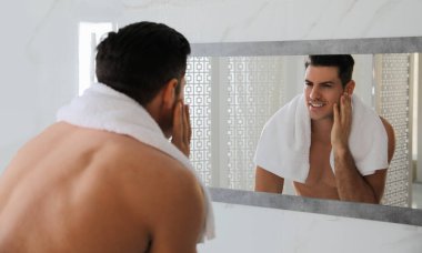 Yakışıklı adam banyoda aynanın yanında tıraş olduktan sonra pürüzsüz yüzüne dokunuyor.