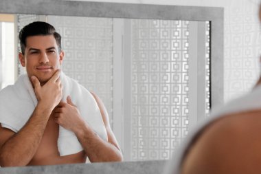 Yakışıklı adam banyoda aynanın yanında tıraş olduktan sonra pürüzsüz yüzüne dokunuyor.