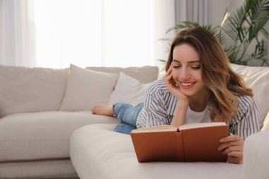 Evdeki kanepede kitap okuyan genç bir kadın.