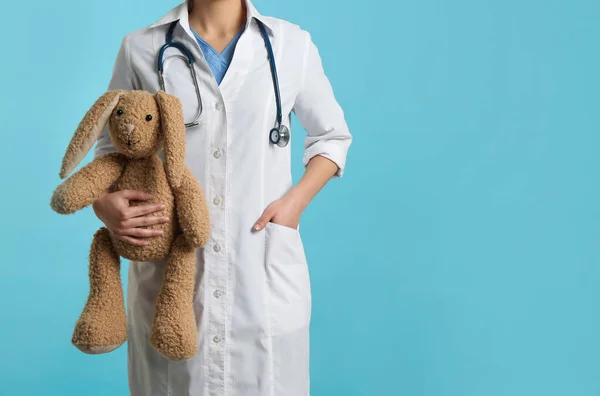 Pediatrician with toy bunny and stethoscope on turquoise background, closeup. Space for text