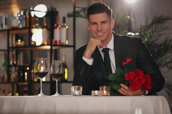 Happy man with roses waiting for his girlfriend in restaurant on Valentine\'s day