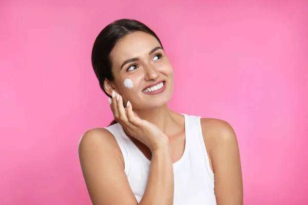 Jonge Vrouw Het Aanbrengen Van Gezichtscrème Roze Achtergrond — Stockfoto