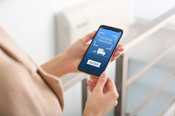 Woman tracking parcel via smartphone indoors, closeup