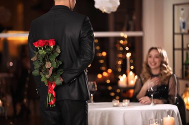 Sevgililer Günü yemeğinde restoranda sevgilisine gül saklayan bir adam.