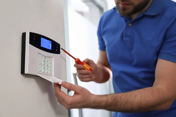 Man installing home security system on white wall in room, closeup