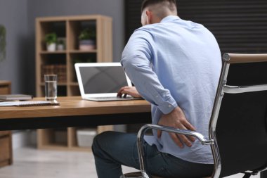 Dizüstü bilgisayarla çalışırken sırt ağrısı çeken bir adam. Kötü duruş belirtileri