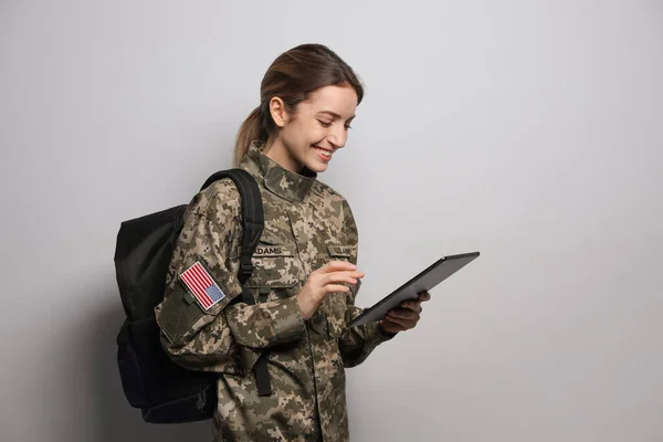 ライトグレーの背景にバックパックとタブレットを持つ女性士官候補生 軍事教育 — ストック写真