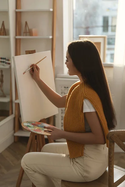 漂亮的年轻女子在家里的画架上画画 — 图库照片