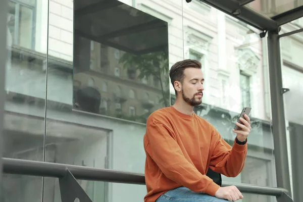 Ung Man Med Smartphone Väntar Kollektivtrafik Vid Busshållplatsen — Stockfoto