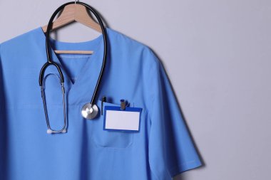 Doktor gömleği steteskop, rozet ve açık gri arka planda asılı kalem. Metin için boşluk