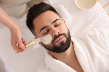 Kozmetik uzmanı spa salonunda adamın yüzüne maske takıyor.