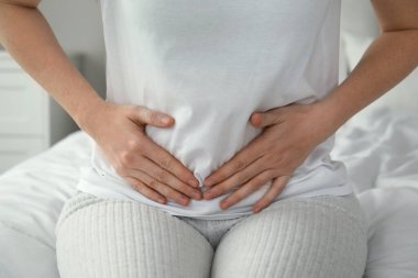 Karın ağrısı çeken bir kadın evinde yatıyor, yakın plan.