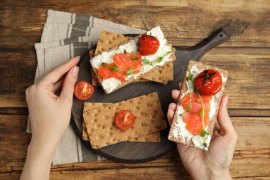 Ahşap masada taze çavdar gevreği, somon, krem peynir ve domates yiyen bir kadın.