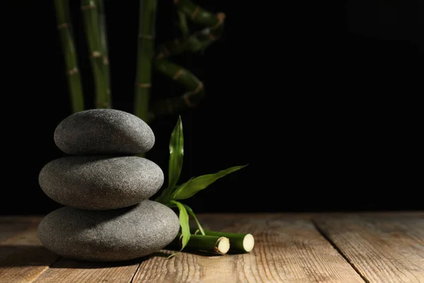 Spa stones and bamboo stems on wooden table against dark background, space for text