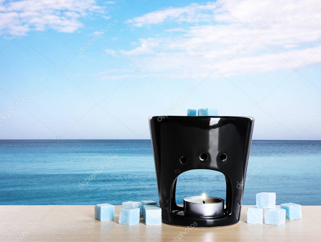 Stylish aroma lamp with wax cubes on wooden table near sea, space for text