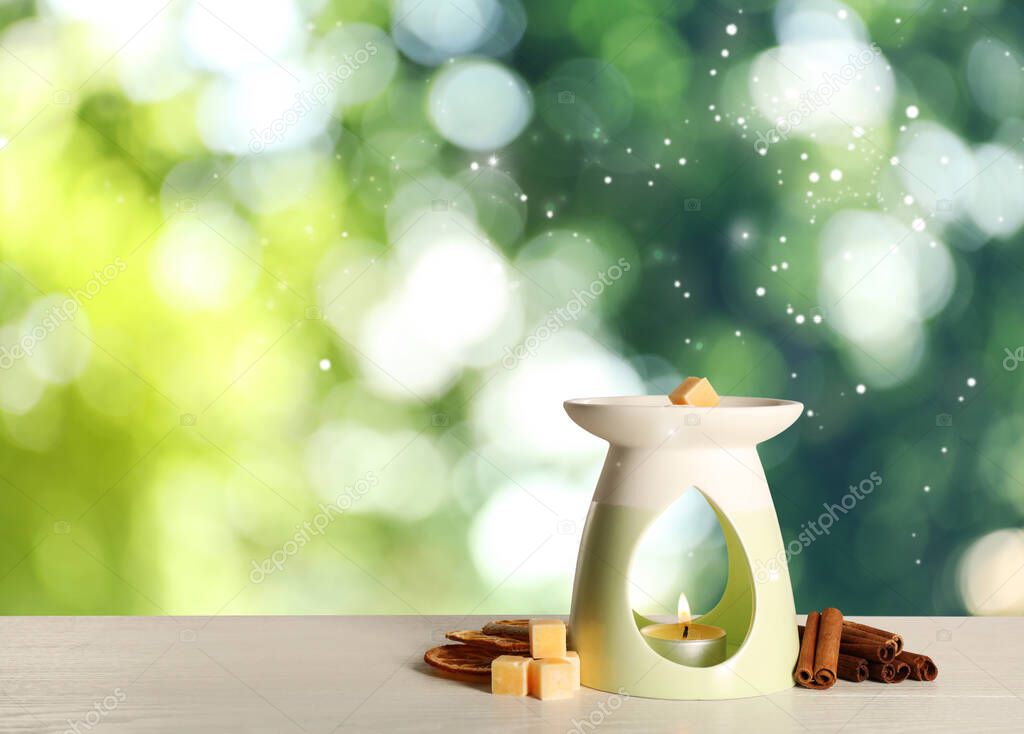 Stylish aroma lamp with essential wax cubes, dried orange slices and cinnamon on white wooden table outdoors, space for text. Bokeh effect