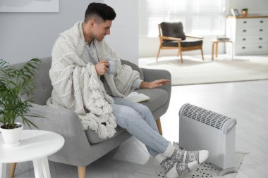 Evdeki elektrikli ısıtıcının yanındaki koltukta oturan mutlu adam.