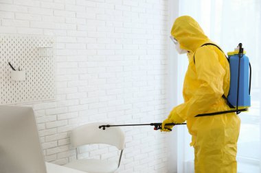 Koruyucu giysili bir çalışan ofisi sterilize ediyor. Tıbbi dezenfeksiyon