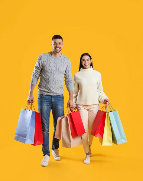 黄色の背景に紙袋を持つ幸せなカップル クリスマスショッピング — ストック写真