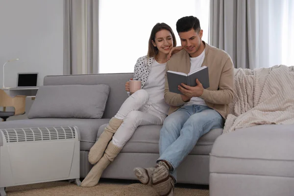 一对快乐的夫妇坐在家里电热器旁边的沙发上 — 图库照片