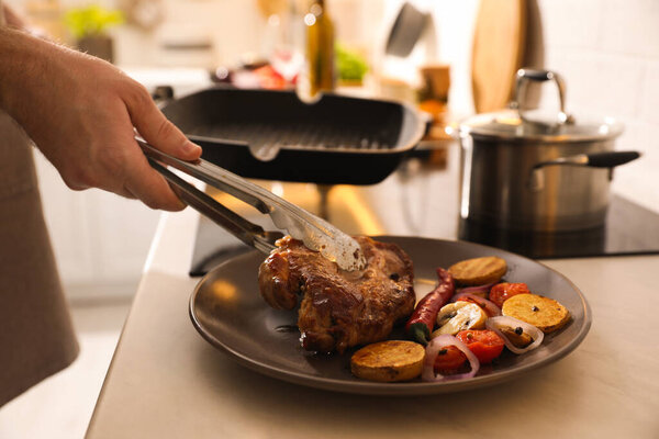 Man putting meat into plate with vegetables cooked on frying pan, closeup