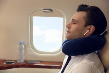 Yolculuk yastığı olan genç adam uçuş sırasında uçakta müzik dinlerken dinleniyor.