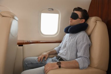 Seyahat yastığı ve maskeli genç adam uçuş sırasında uçakta uyuyor.